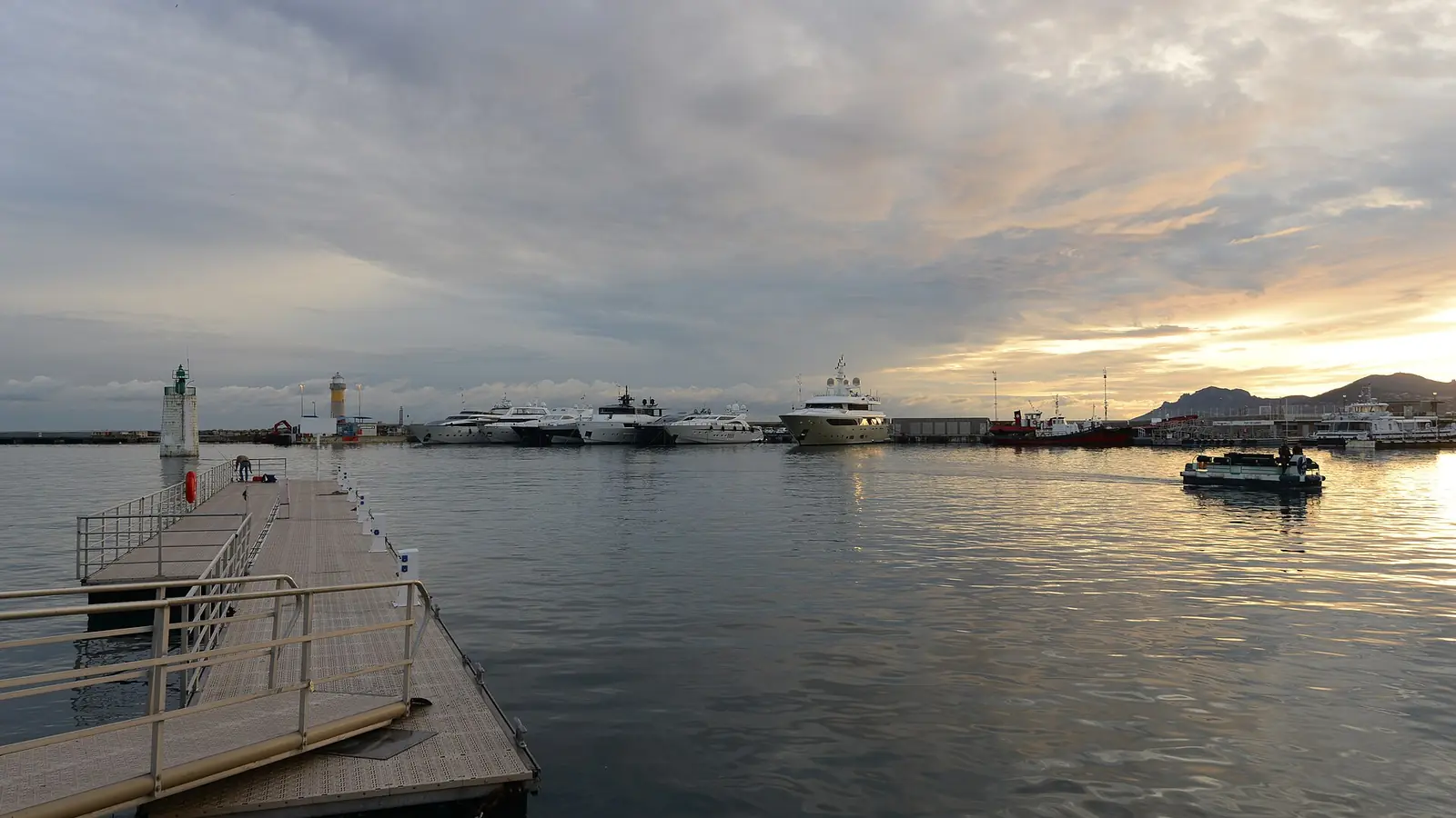 Harbour entrance at dusk with a large yacht lying off the pier head
